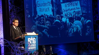 padeluun am Redner.innenpult. Im Hintergrund ein Foto einer Demo.