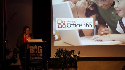 Leena Simon am Redner.innenpult. Im Hintergrund ein Werbefoto von Office 365.