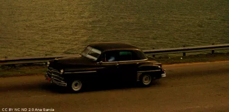 Ein Oldtimer auf einer Straße nahe einem Gewässer (Foto in Sepia-Färbung).