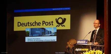 Das Logo der Deutschen Post ist per Beamer an die Wand geworfen. Sönke Hilbrans steht am Redner.innenpult.