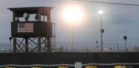 Überwachungsturm mit einer US-Flagge hinter einer Mauer mit Stacheldraht.