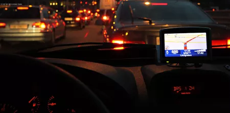 Point of view: Fahrer.innensitz eines Autos. Stau auf der Straße. Es ist dunkel. Ein Navi leuchtet.